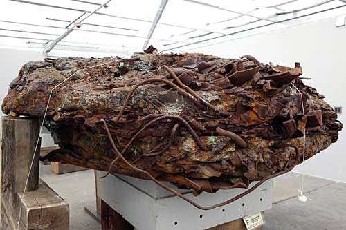 Figure 32. The 'Meteorite' that was once preserved in Hangar 17 of John F. Kennedy International Airport (JFK) for WTC remains. High-density fused agglomeration of resolidified ferrous metal and concrete aggregate with embedded paper documents, showing heterogeneous composite artifact.
  <br>
  - Photos by Lane Johnson