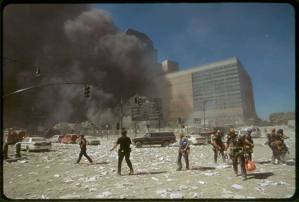 Figure 76. (9/11/01) A block north from the WTC complex, looking west across the intersection of Murray & West Streets, course dust settles, while fine dust rises above the feet. Debris pile exhibiting continuous athermal aerosol emission with particulate wafting upward without wind or heat, demonstrating dielectrophoretic levitation
