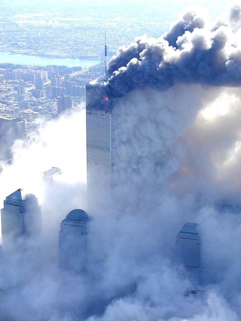 Figure 14. (9/11/01) WTC1 showing white/gray particulate cloud emission along vertical building face prior to structural failure, exhibiting rapid volumetric expansion.
  <br>
  - Photo by Det Greg Semendinger, NYC Police Aviation Unit