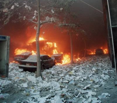 Figure 56. (9/11/01) West Broadway: vehicles burning near trees with paper debris on ground remaining unburned; trees and paper intact while nearby vehicles show selective oxidation, demonstrating paper survival next to burning steel
